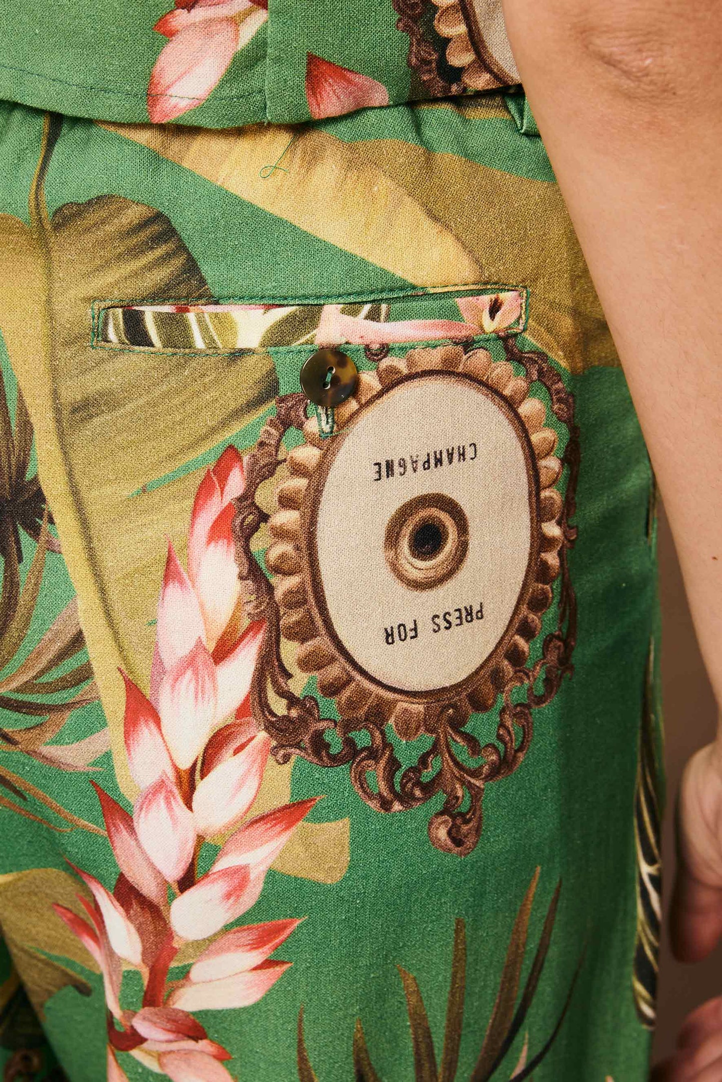 Calça Porto Papel de Parede verde, tecido texturizado, estampa tropical floral. Botão "Press for Champagne".