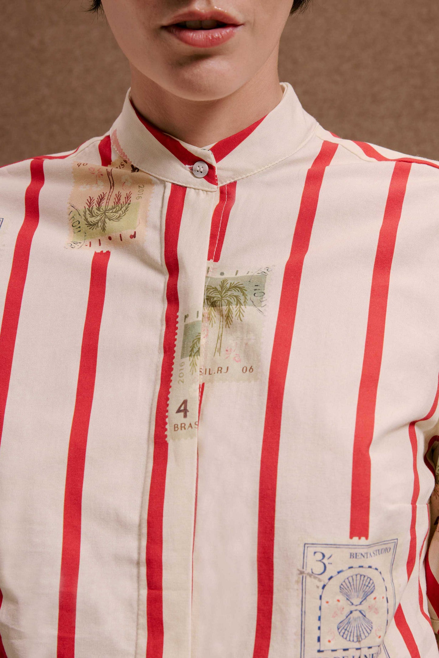 Blusa Roma creme com listras verticais vermelhas e estampas de selos vintage: palmeiras, conchas e carimbos.
