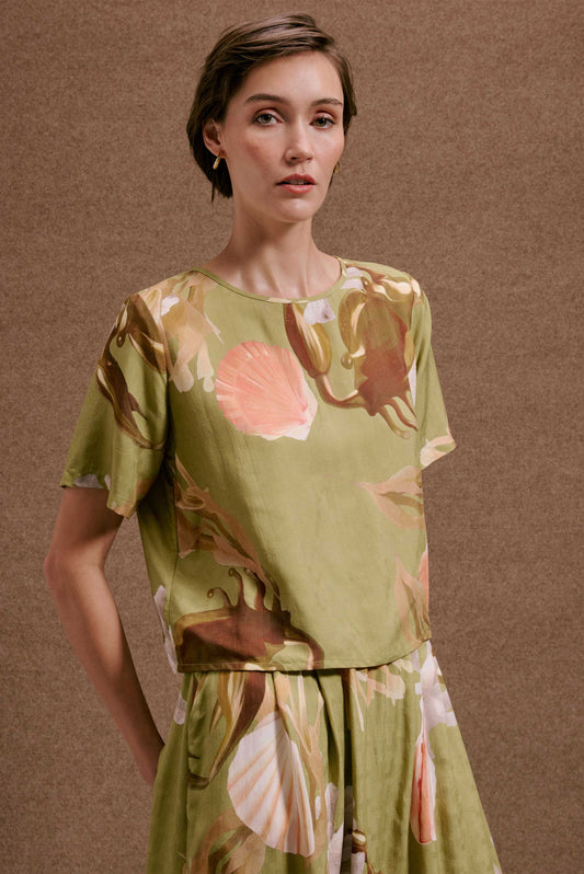 Blusa Nápoles Lembranças Verde, manga curta, estampa de conchas e folhagens verde, rosa e marrom, texturizada.