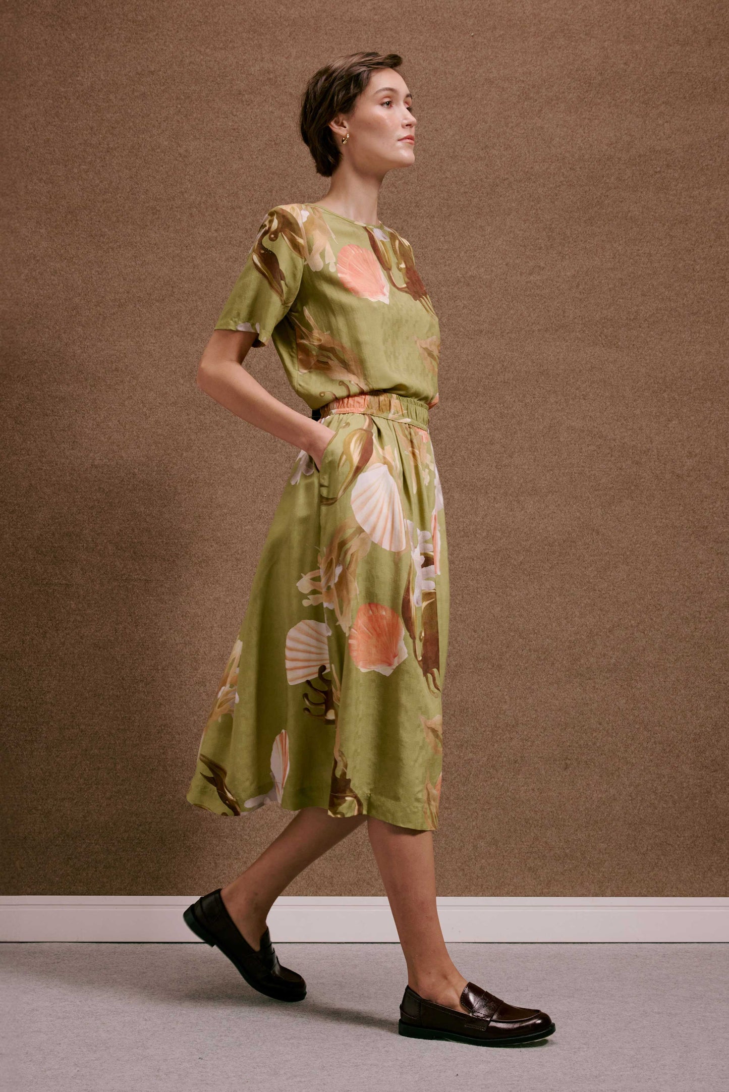 Vestido midi Saia Rodada Lembranças Verde. Estampa de conchas e corais em tons quentes sobre tecido verde oliva.