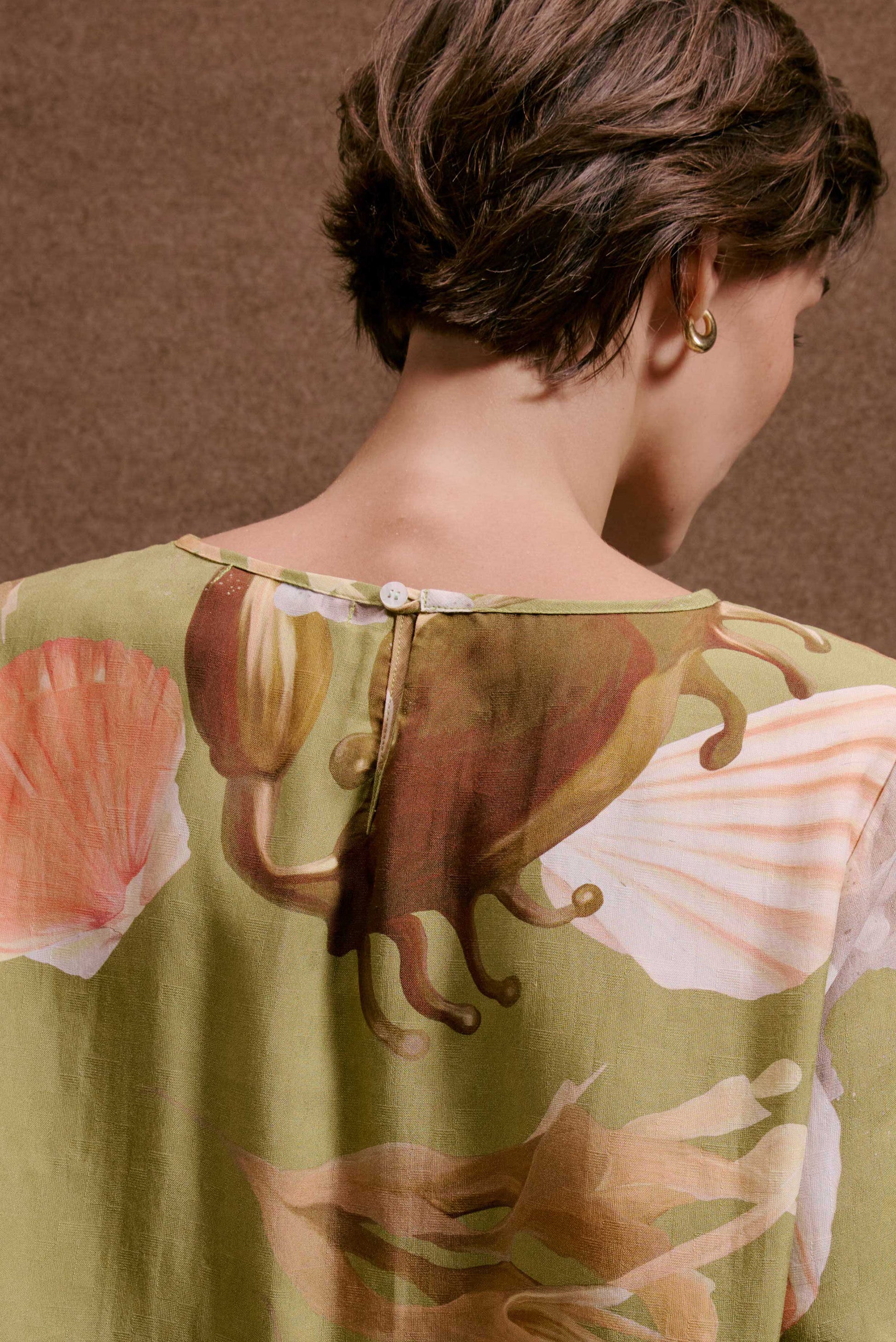 Blusa Nápoles Lembranças Verde. Costas de blusa verde-oliva com estampa marinha de caranguejo e conchas, tecido texturizado.