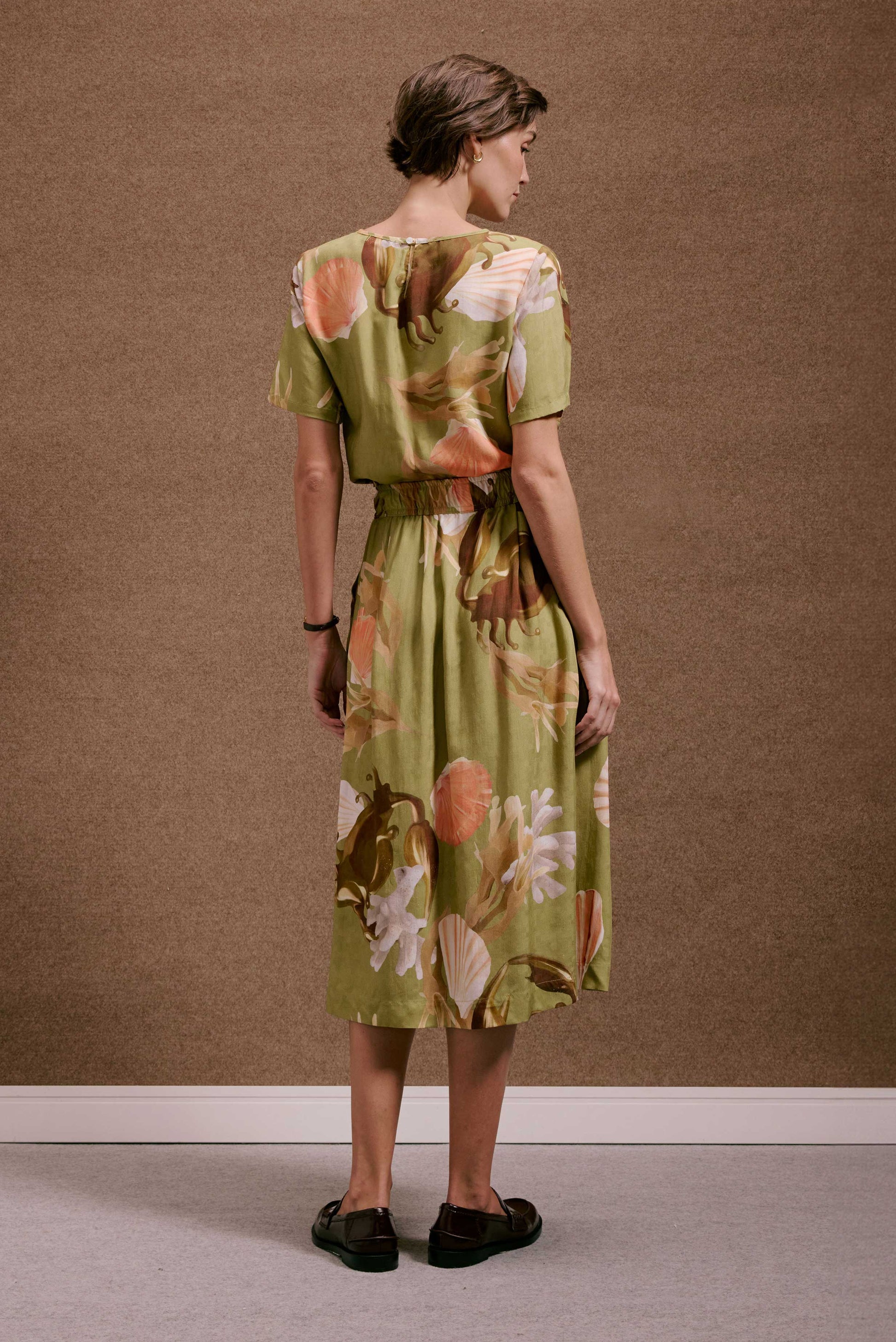 Saia Rodada Lembranças Verde com estampa de conchas e corais em tons alaranjados e terrosos, caimento leve e fluido.