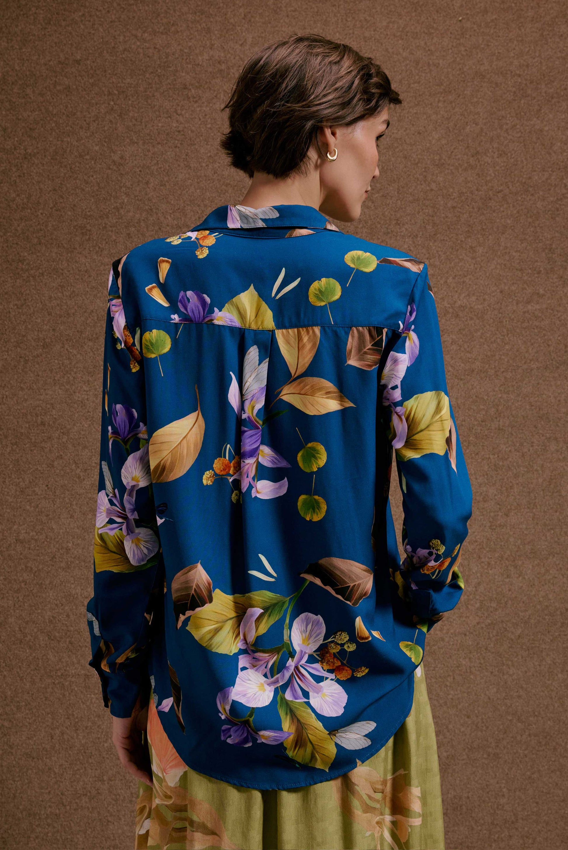 Camisa ML Anoitecer Botânica azul vibrante, com estampa de flores roxas e folhas amarelas, vista de costas em fundo marrom.