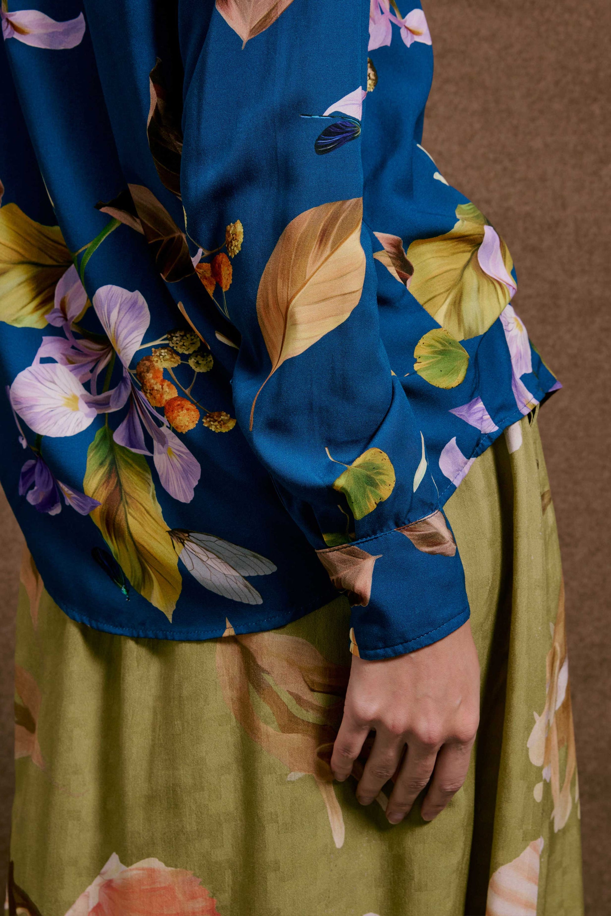 Camisa ML Anoitecer Botânica, azul com estampa de flores roxas, folhas douradas e insetos; saia verde-oliva.