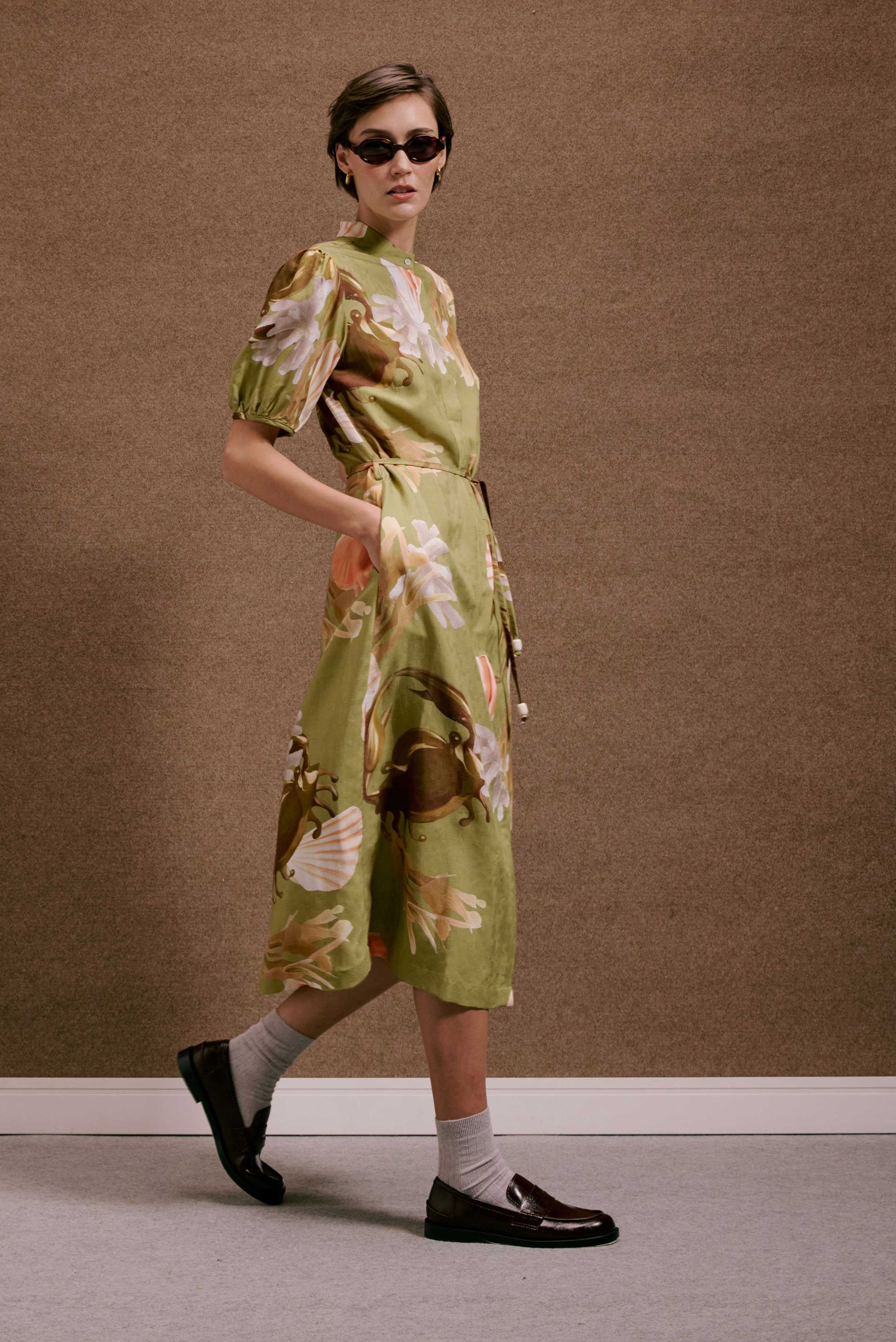 Vestido Roma Lembranças midi verde com estampa de plantas e conchas em tons terrosos, mangas bufantes, cinto e bolsos.