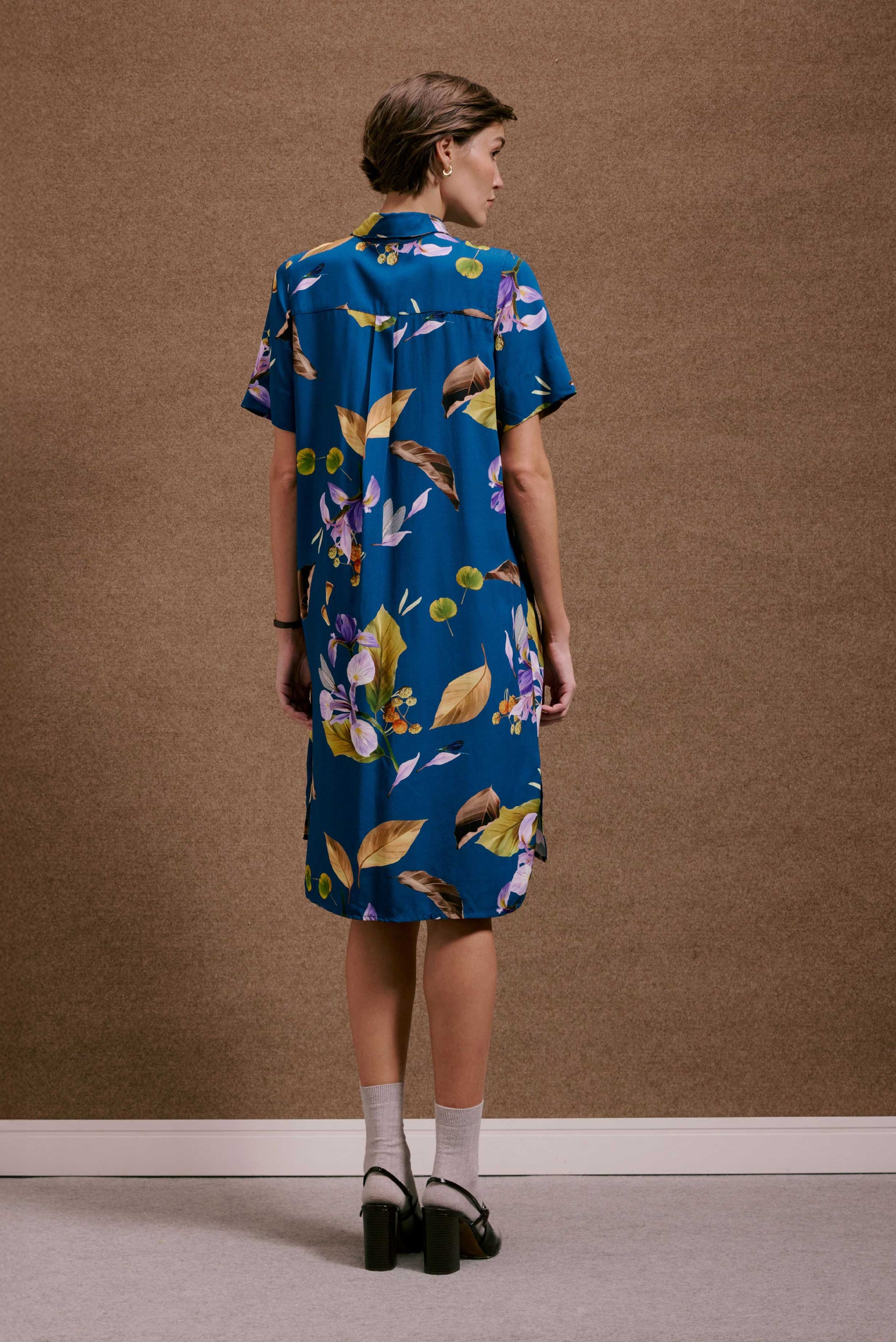 Chemise Fenda Anoitecer Botânica azul, estampa de folhas e flores roxas e terrosas. Vista traseira, tecido leve.