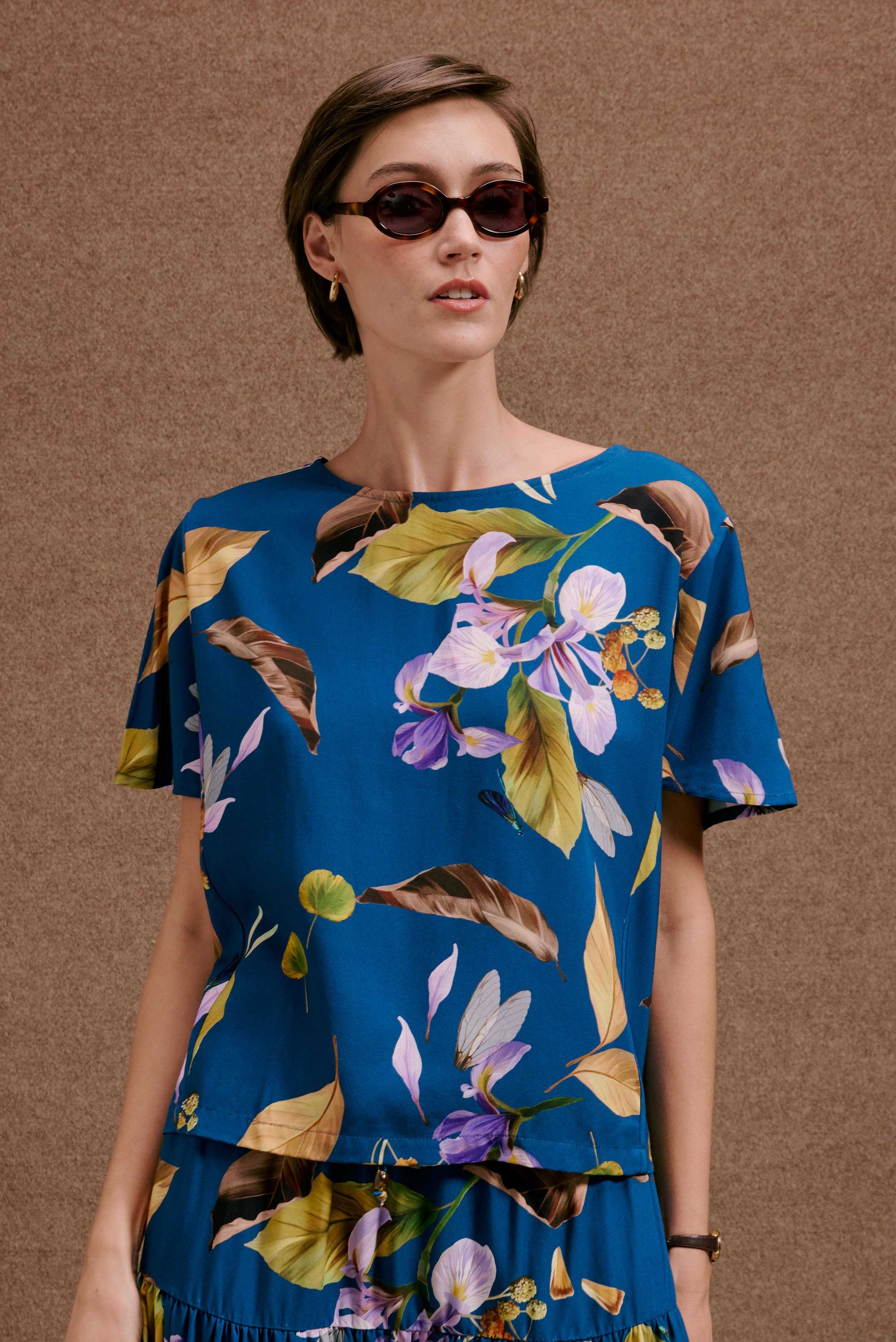 Blusa Japa New Anoitecer Botânica azul-petróleo, manga curta, estampa de flores roxas, brancas e folhagem.