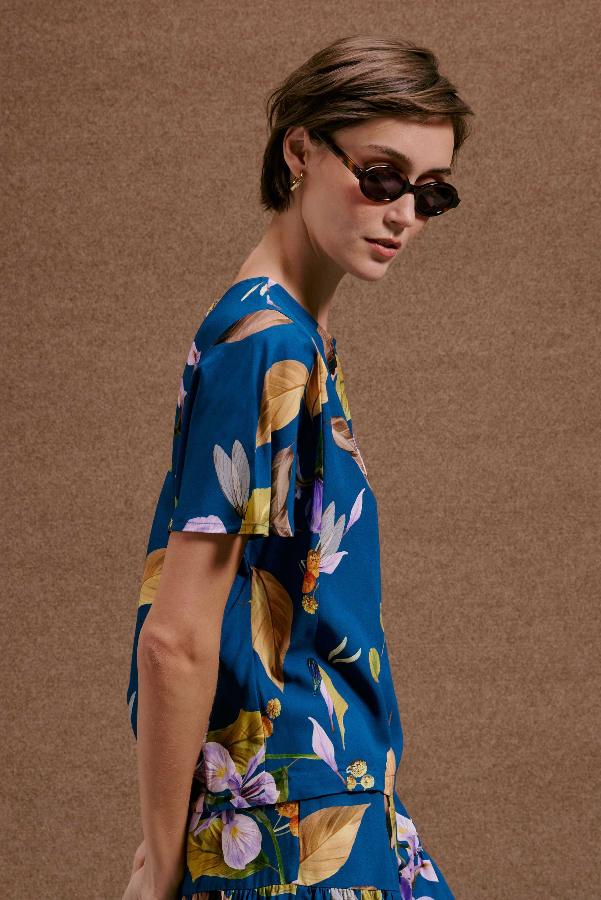 Blusa Japa New Anoitecer Botânica azul vibrante, estampa botânica com flores roxas. Modelo com óculos escuros.