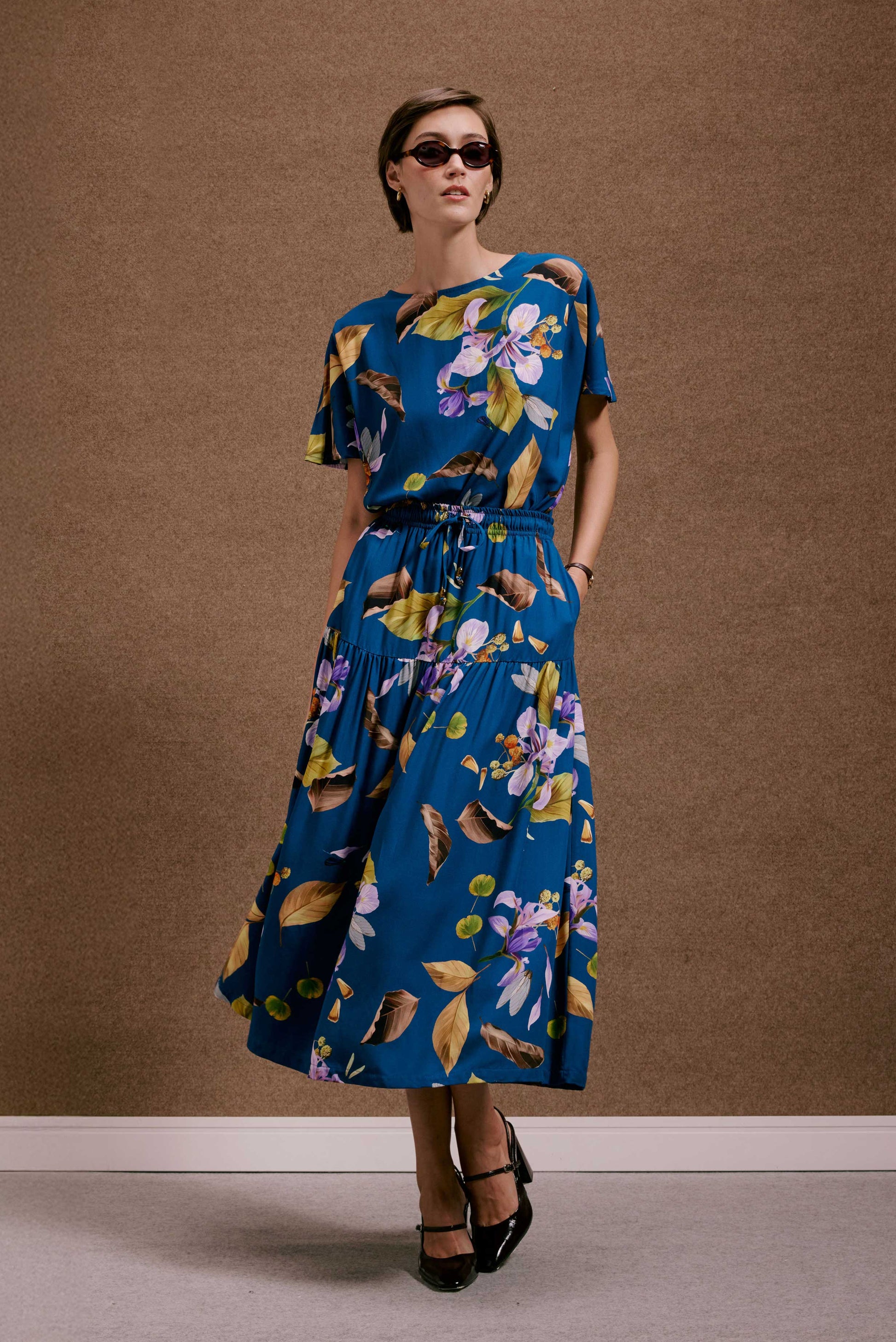 Vestido azul midi com estampa botânica 'Saia Gipsy Anoitecer Botânica'. Modelo fluido de mangas curtas e cintura elástica.