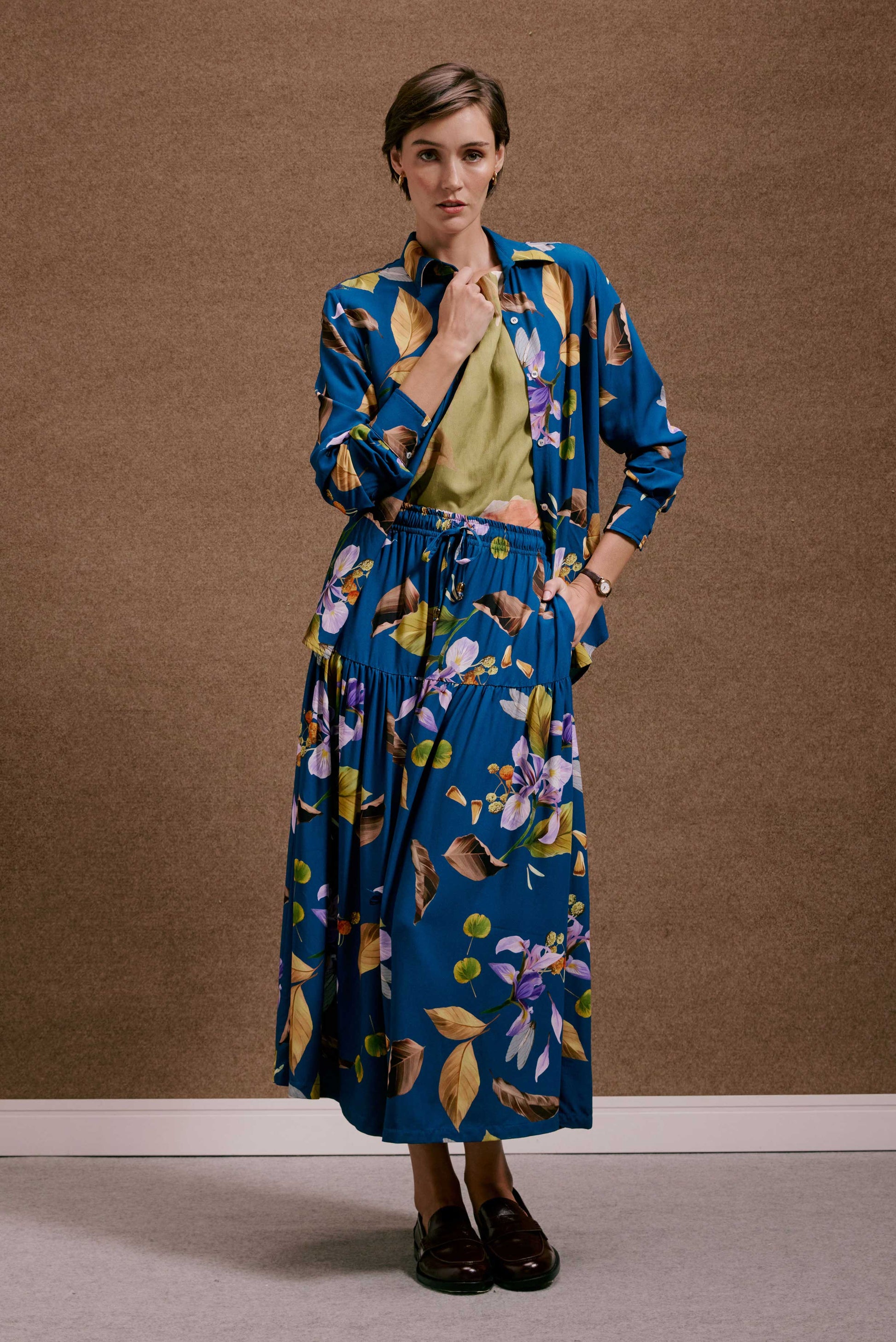 Saia Gipsy Anoitecer Botânica: Saia longa azul com estampa botânica de folhas e flores roxas e amarelas. Estilo gipsy fluido.
