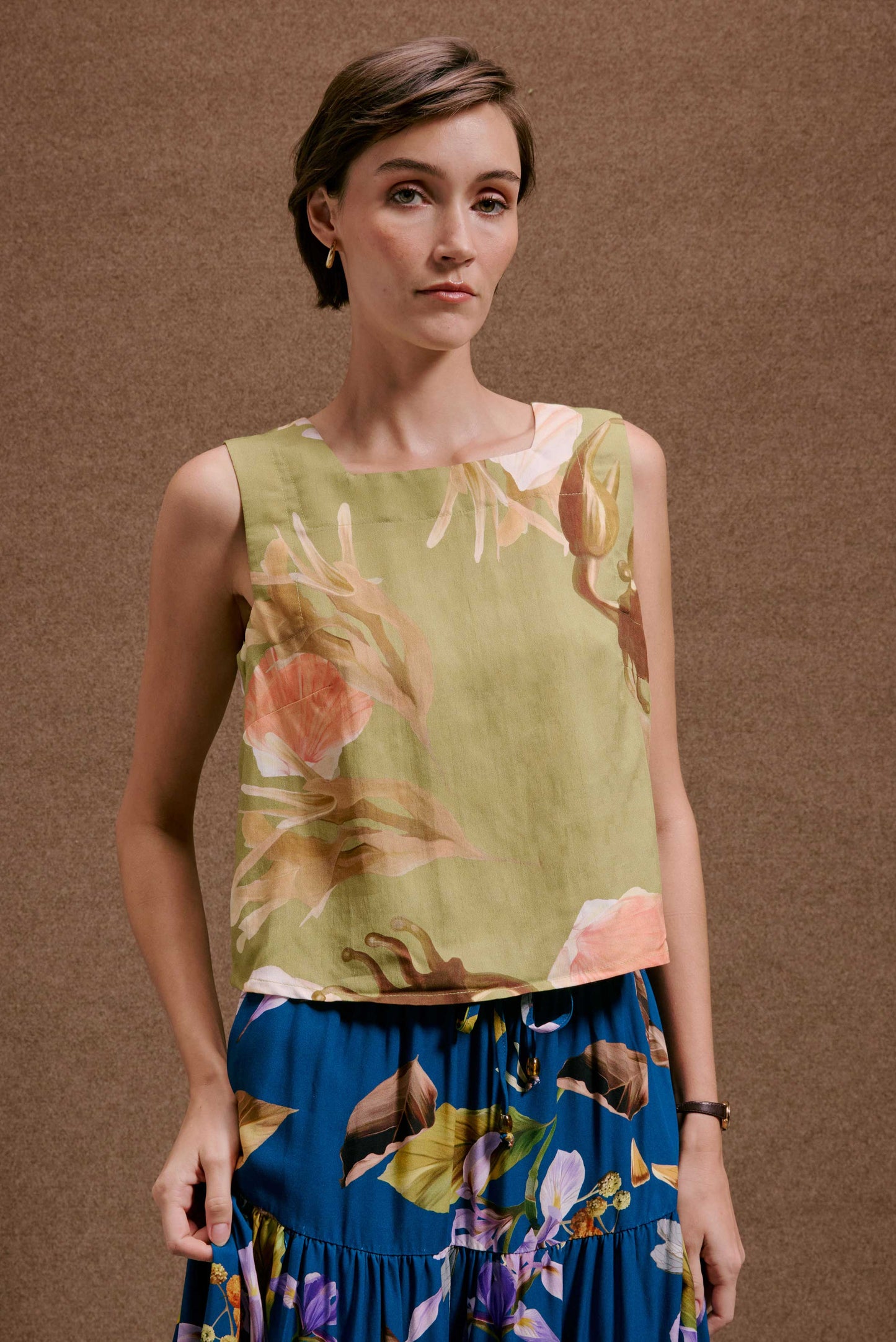 Blusa Quadradinha Lembranças Verde floral, decote quadrado, em tons laranja e marrom, tecido leve, sobre saia azul estampada.