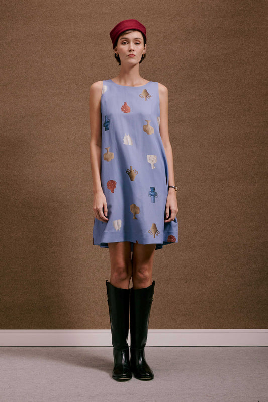 Vestido Marais Vasinhos Mini azul claro de tecido liso, sem mangas, com estampa de vasos coloridos. Modelo com boina e botas.