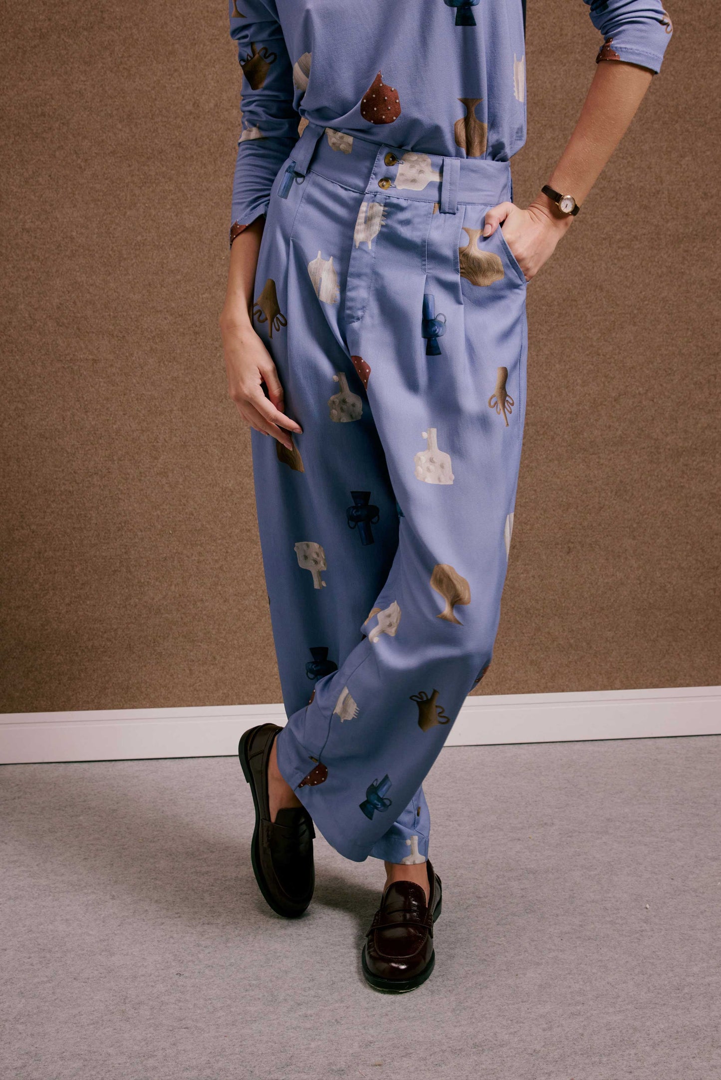 Calça Porto Vasinhos Mini azul celeste, cintura alta, com estampa de vasos terrosos e abstratos. Tecido leve e liso.