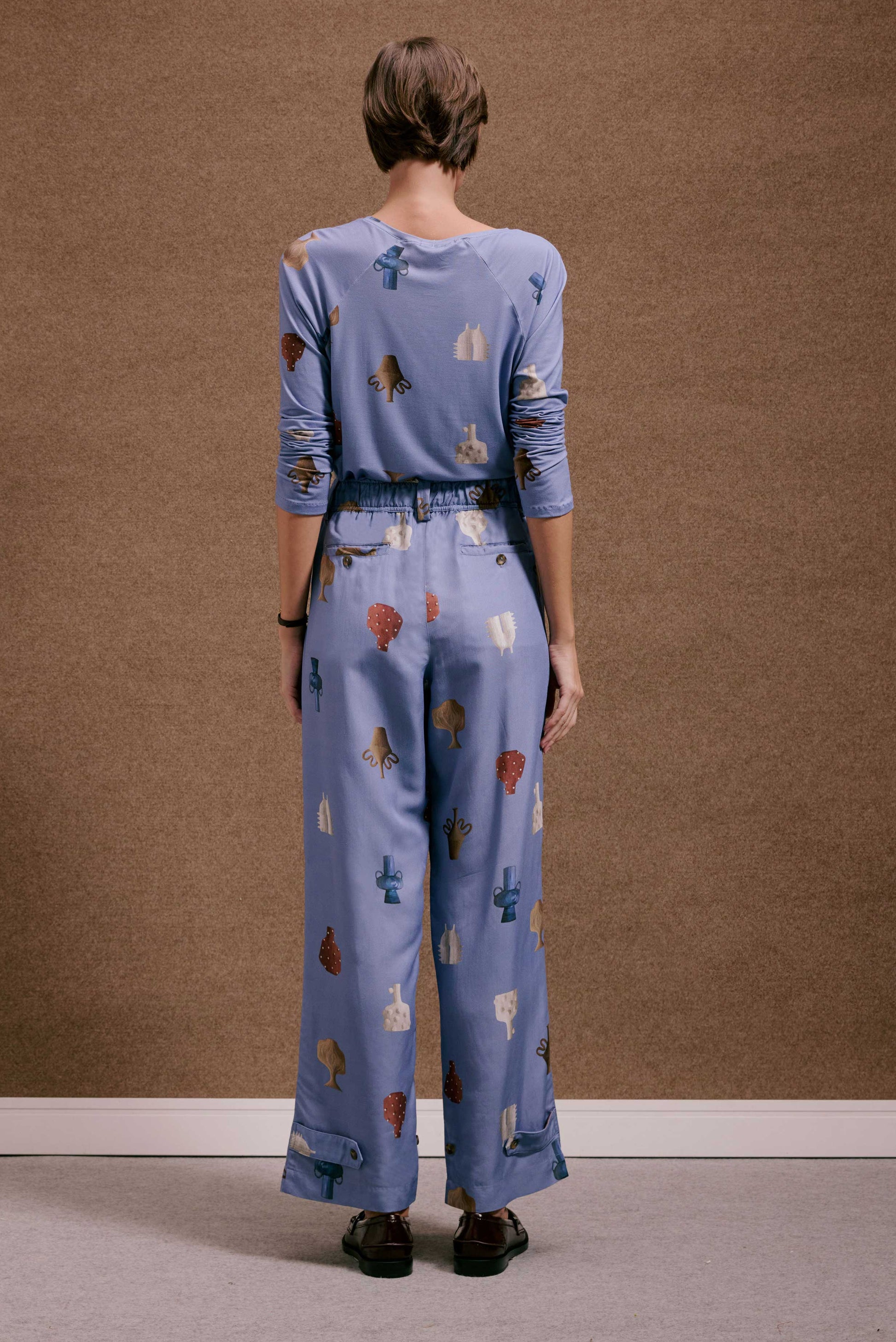 Calça Porto Vasinhos Mini e blusa azul acinzentado com estampa de vasos e formas abstratas em tons terrosos.