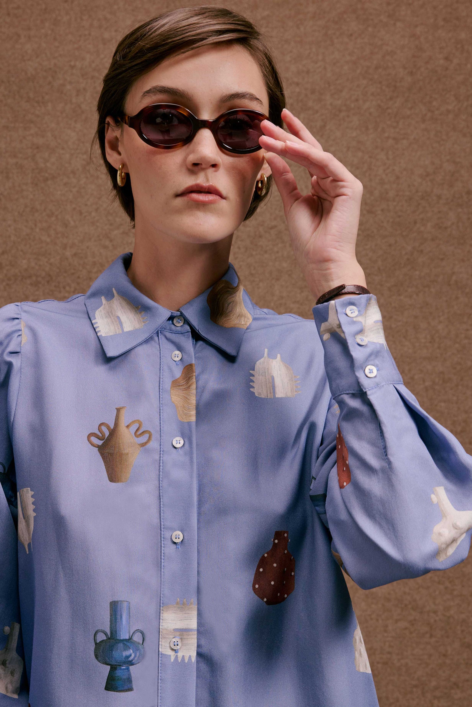 Camisa Studio Vasinhos Mini azul claro, estampa de vasos em tons neutros e terrosos, mangas bufantes, estilo casual chic.