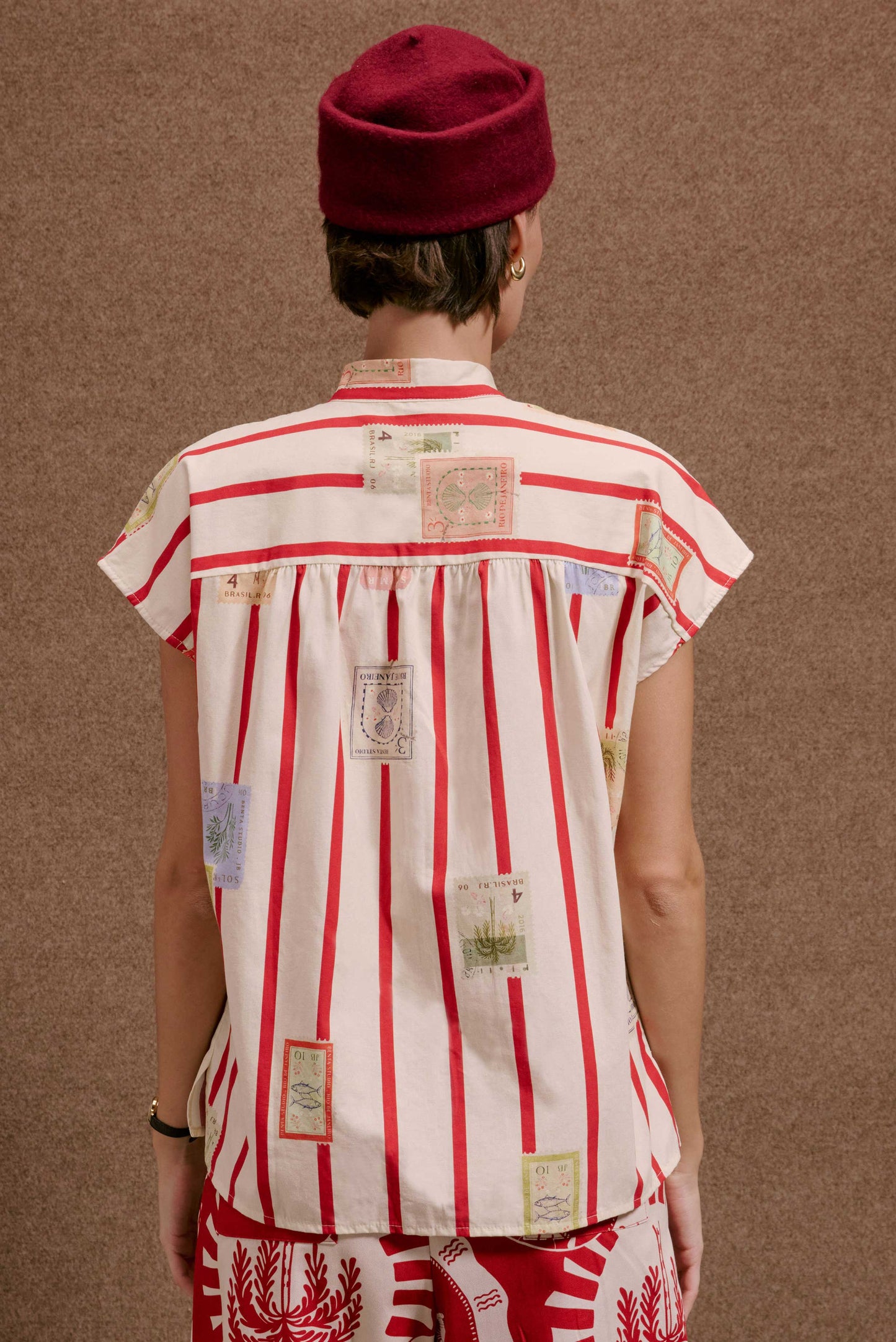 Camisa Gênova Selos Listras: camisa feminina branca com listras vermelhas e estampas de selos de viagem coloridos.