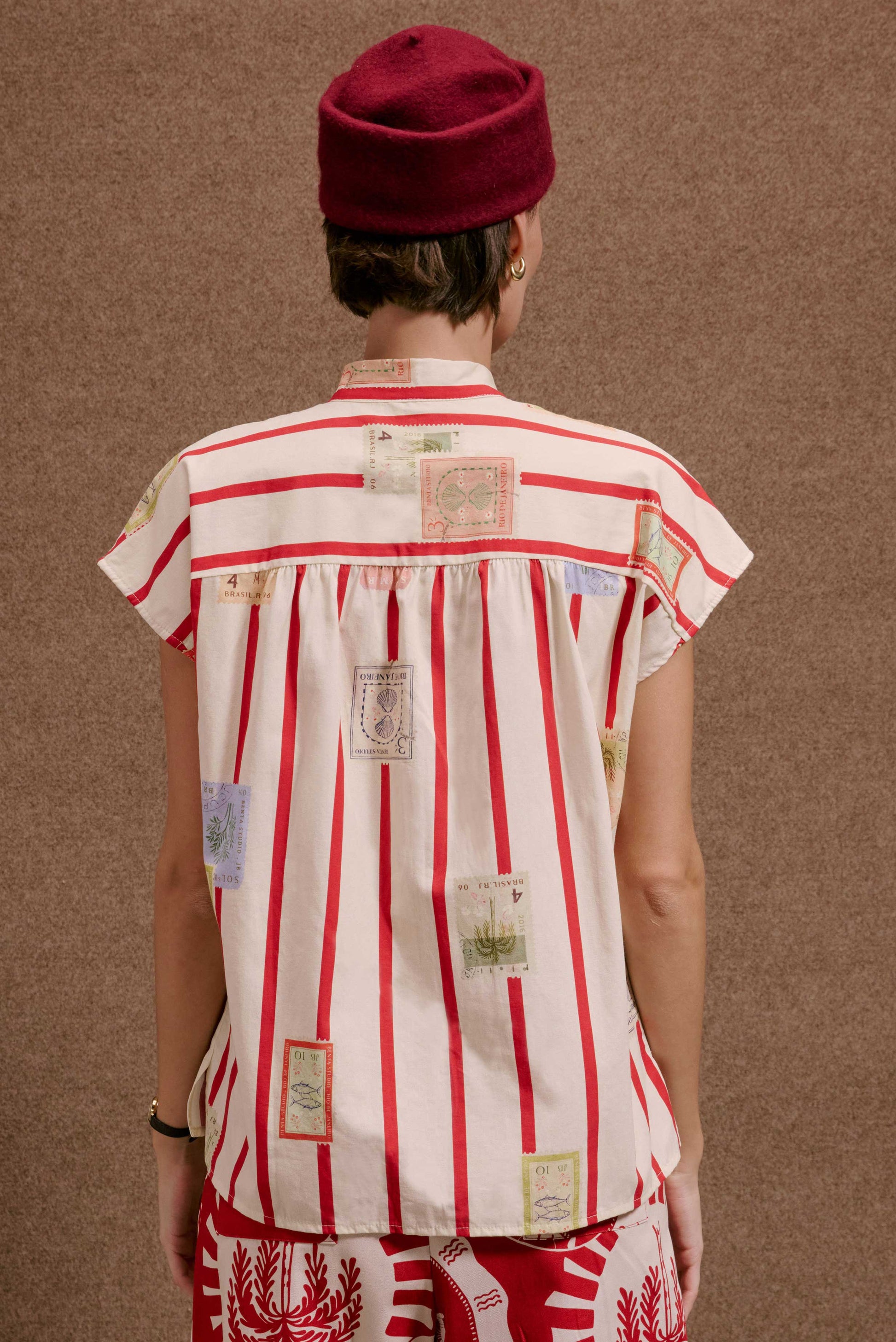 Camisa Gênova Selos Listras: camisa feminina branca com listras vermelhas e estampas de selos de viagem coloridos.