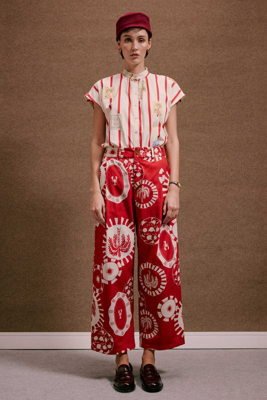 Calça Japão Pratinhos Vermelho, estampa branca com lagostas e palmeiras. Modelo usa camisa listrada vermelha e chapéu.
