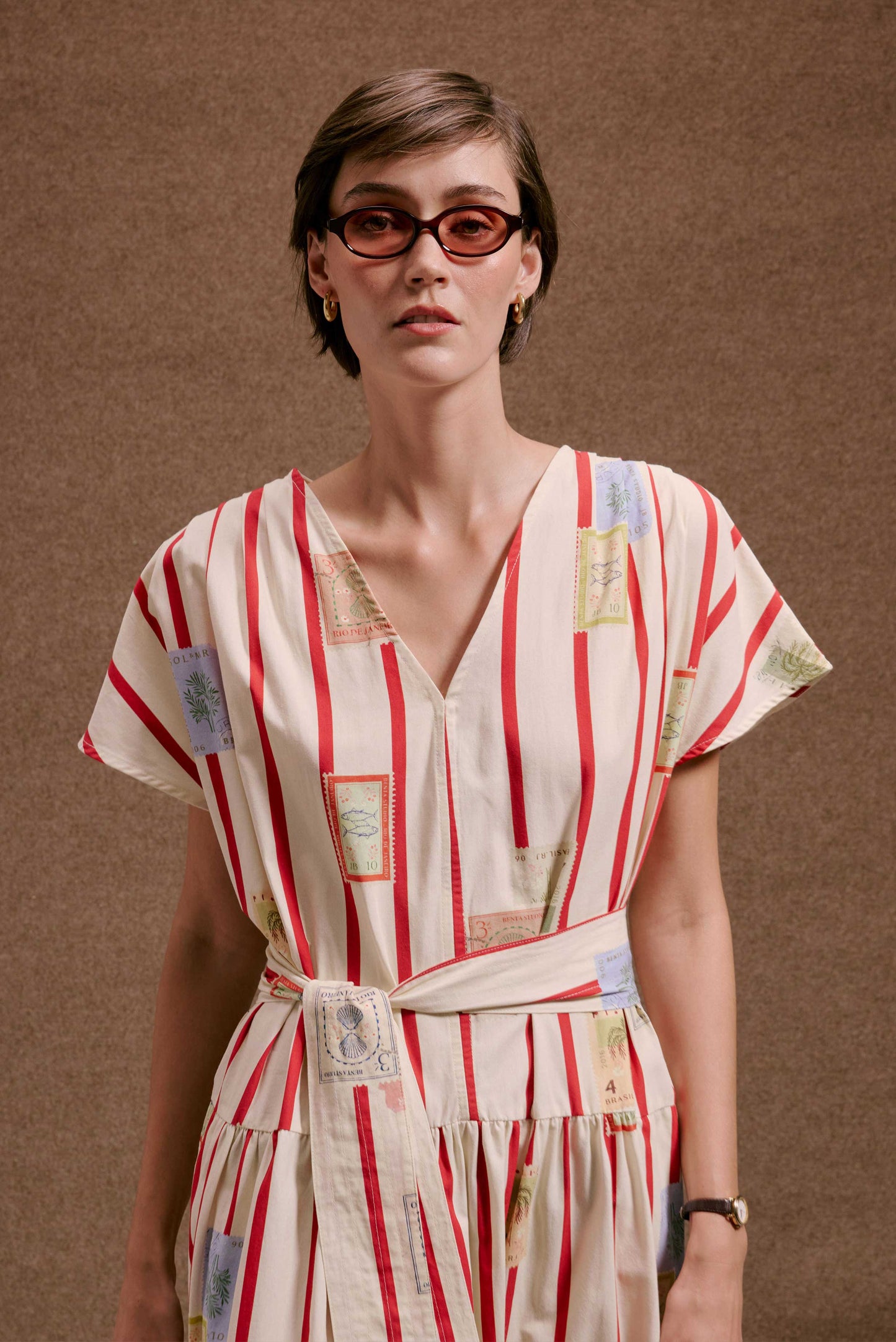 Vestido Galeria Selos Listras off-white com listras vermelhas e estampa de selos, decote V, mangas curtas, faixa na cintura.
