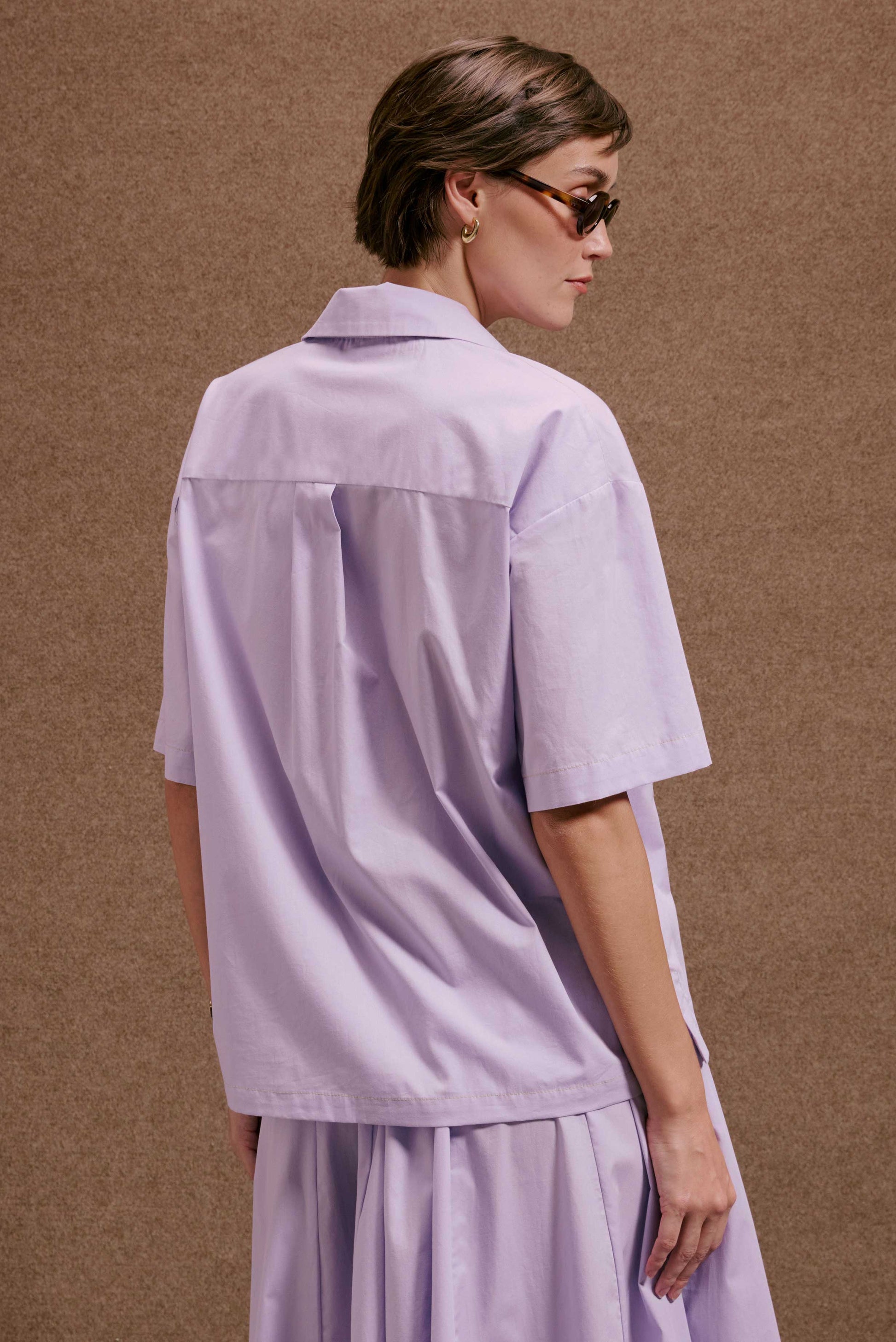 Camisa Havana Orquidário lilás de manga curta, corte solto e prega nas costas. Em tecido leve e liso.