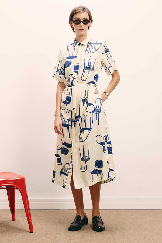 Vestido Paris Cadeiras midi off-white, estilo chemise, com estampa de cadeiras azuis e cinto, calçado com loafers.